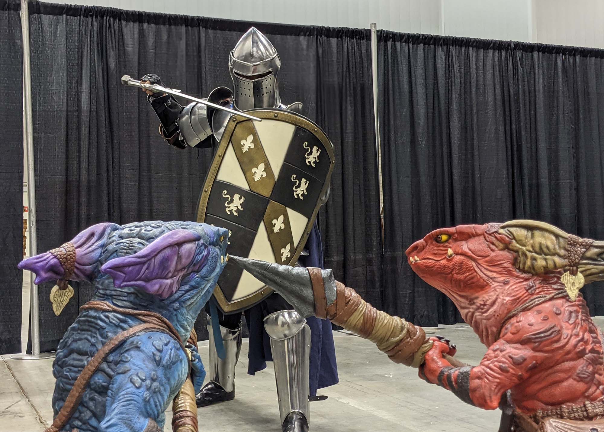A person dressed in knight's armor facing off against two life sized foam kobolds
