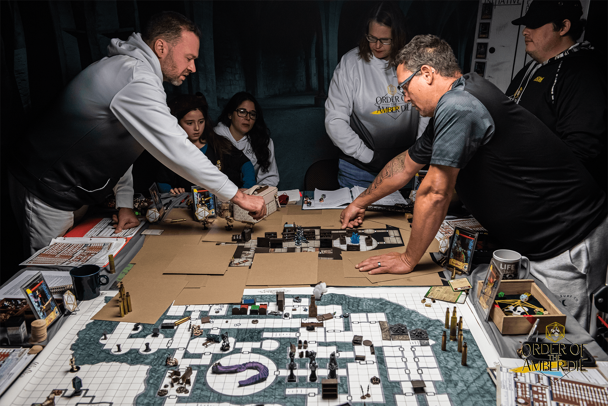 Players all standing and leaning over a table covered in maps and miniatures