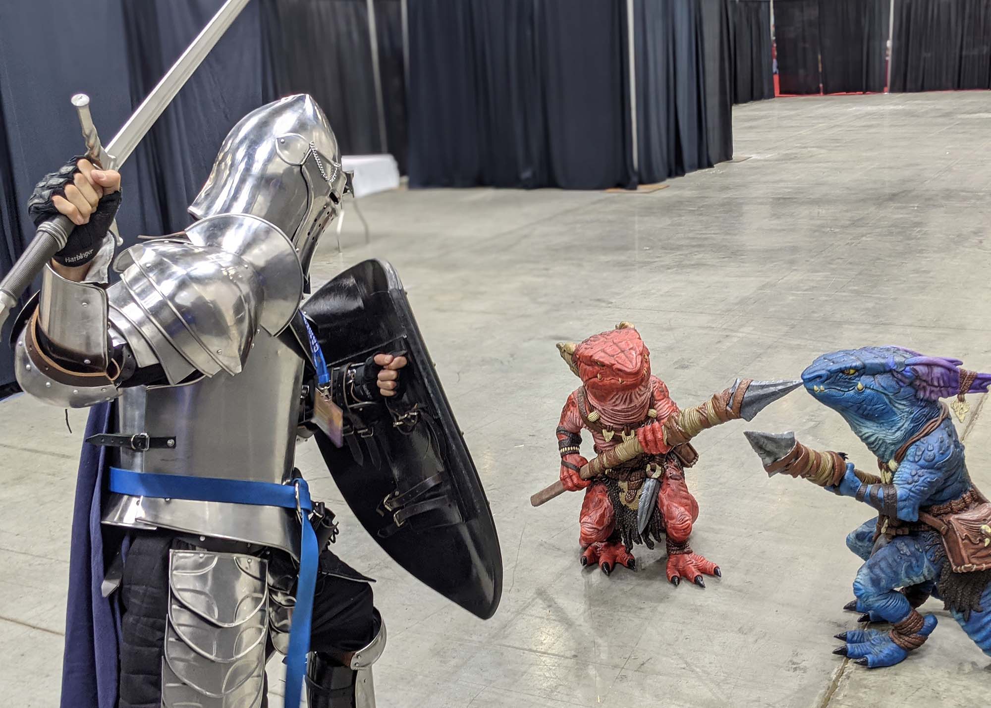 A person dressed in knight's armor facing off against two life sized foam kobolds