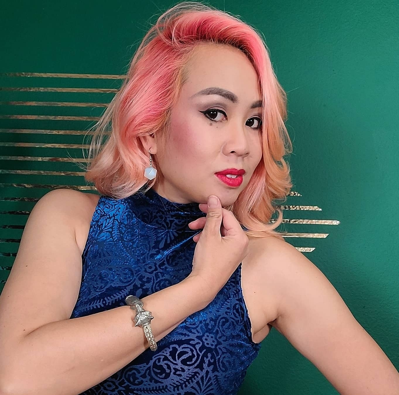 Headshot of Michelle Nguyen Bradley, wearing a blue sleeveless blouse with pink hair over a green background 