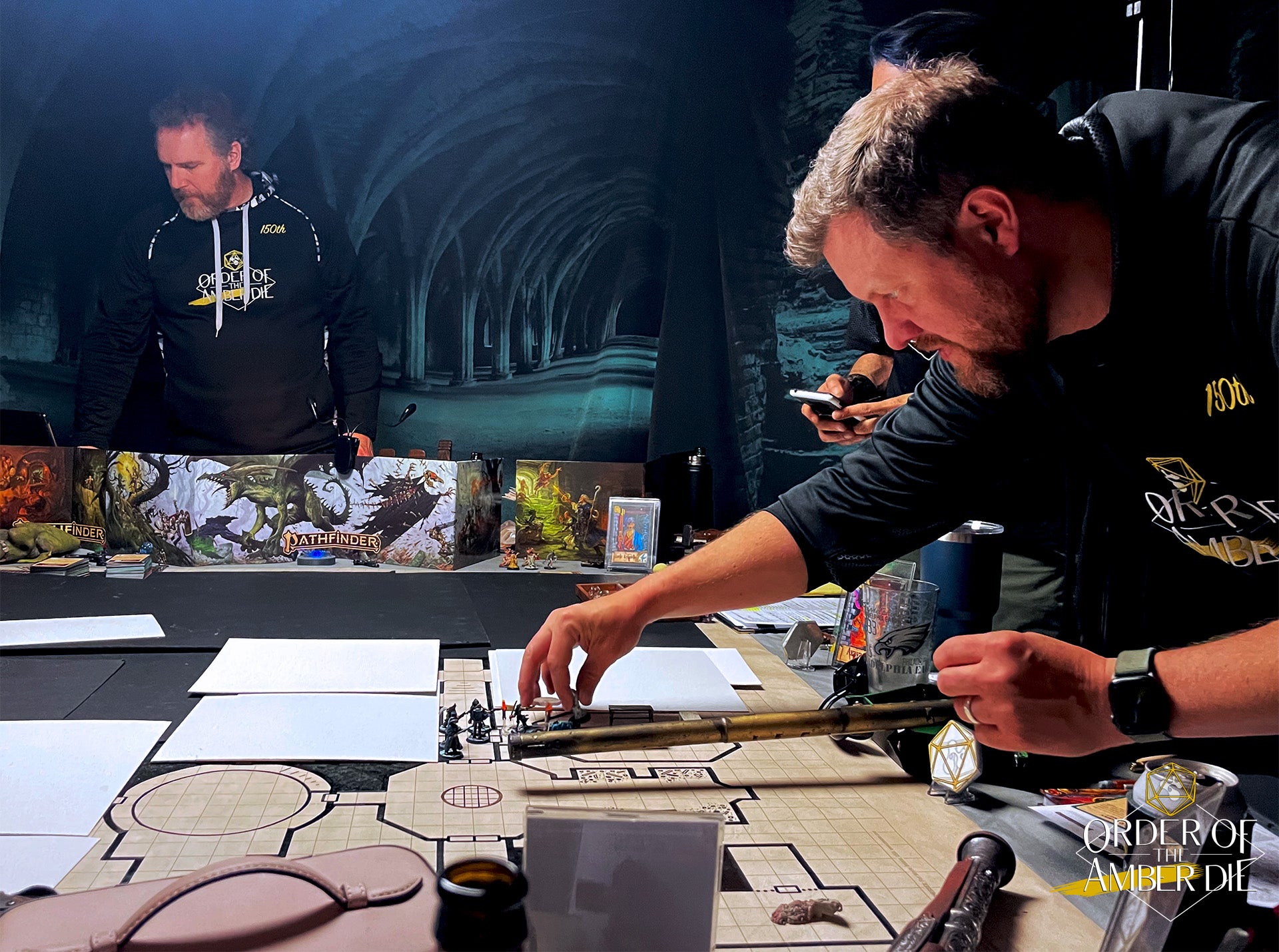 Order of the Amber Die: Players sitting and standing around a gaming table with a covered map