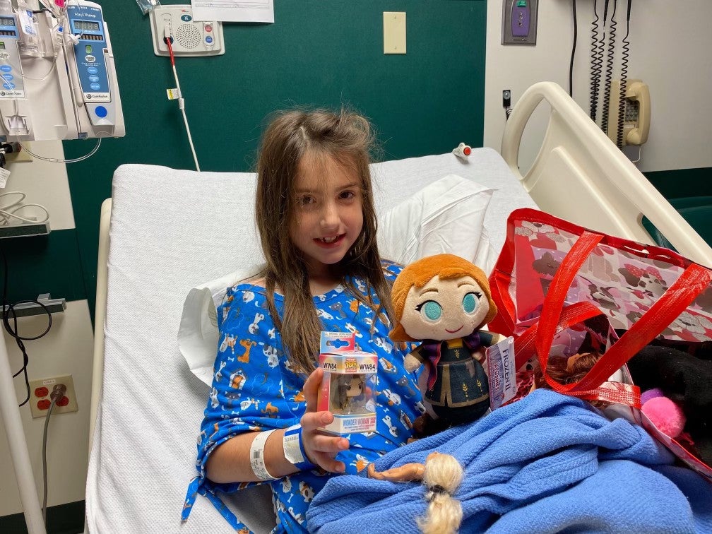 a photo of a smiling kid in a hospital room with an Anna doll and Funko Pop figure