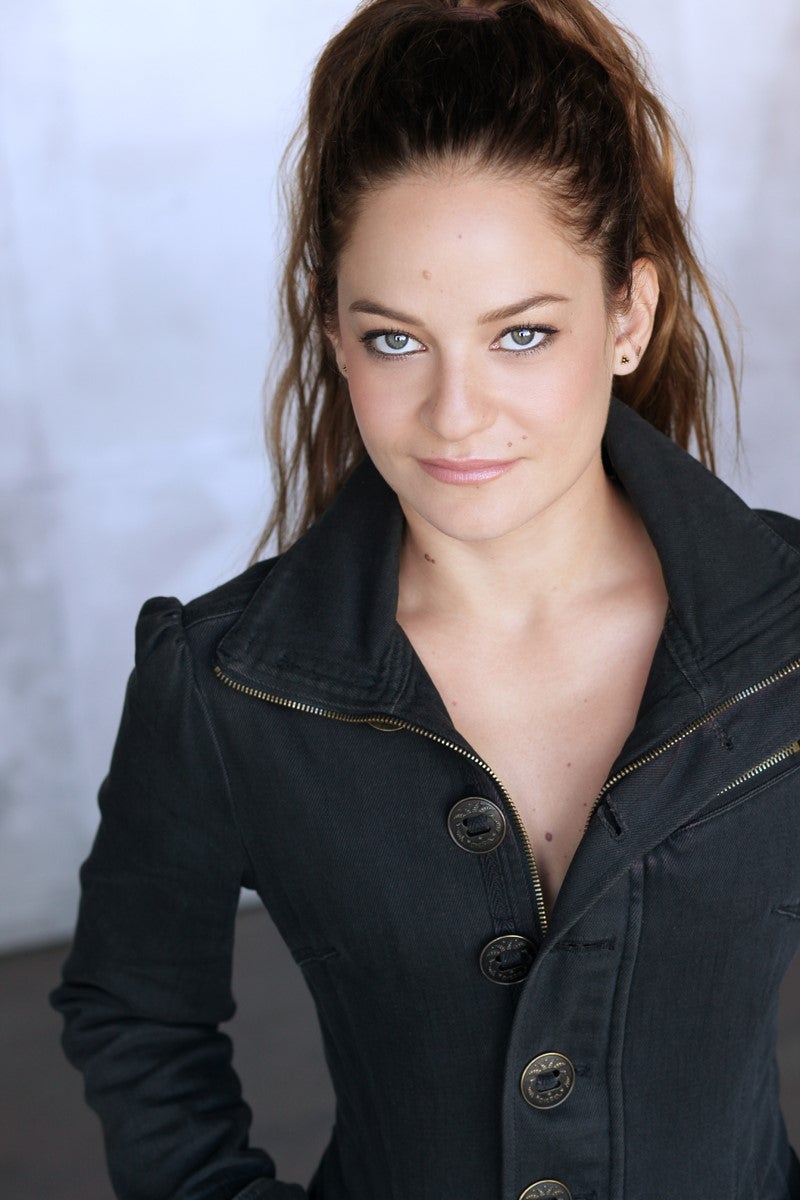 Diana Restrepo headshot, she's standing in front of a textured white background while wearing a black jacket