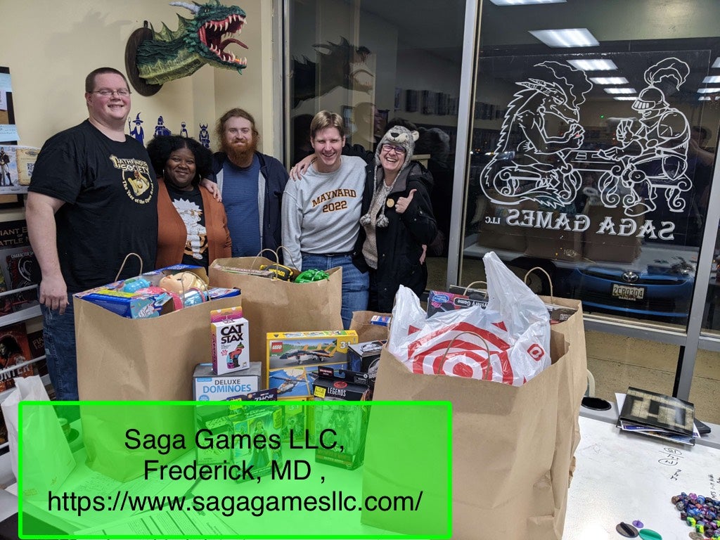 Photo Credit: Zach Davis - a group of volunteers stand behind a table covered in toys for a charity toy drive in Saga Games LCC, in Maryland