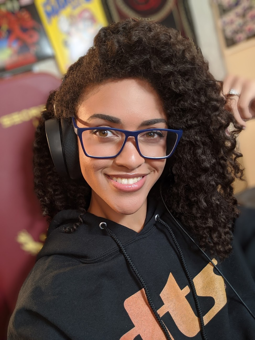 Headshot of Chelsea Bytes, she is wearing glasses and headphones with her curly hair swept to the side