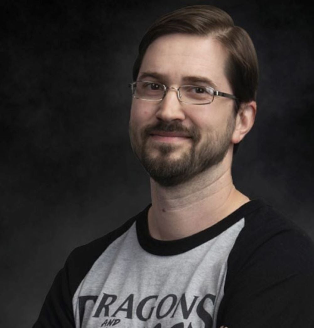 Headshot of Jim Rodehaver, standing in front of a dark background wearing a Dragons and Things t-shirt