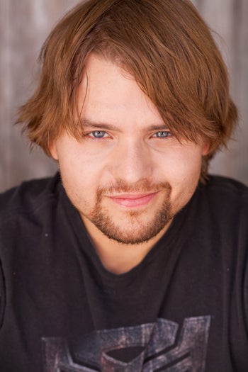 Headshot of Adam Conn, he has red hair and a trimmed beard while wearing a black t-shirt