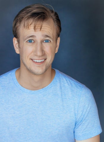 Headshot of Nathan Ondracek, smiling in front of a dark blue background while wearing a light blue t-shirt