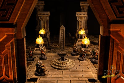 A close up photo of the player character miniatures in a stone temple-like structure with four lit braziers and a small obelisk-like structure in the center of the room