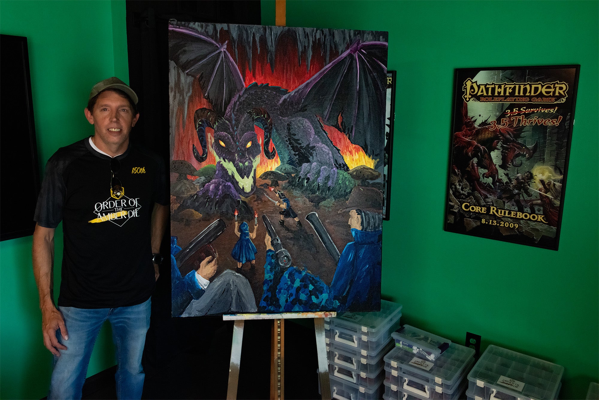 A man standing by a painting of a group of adventurers facing a giant black dragon