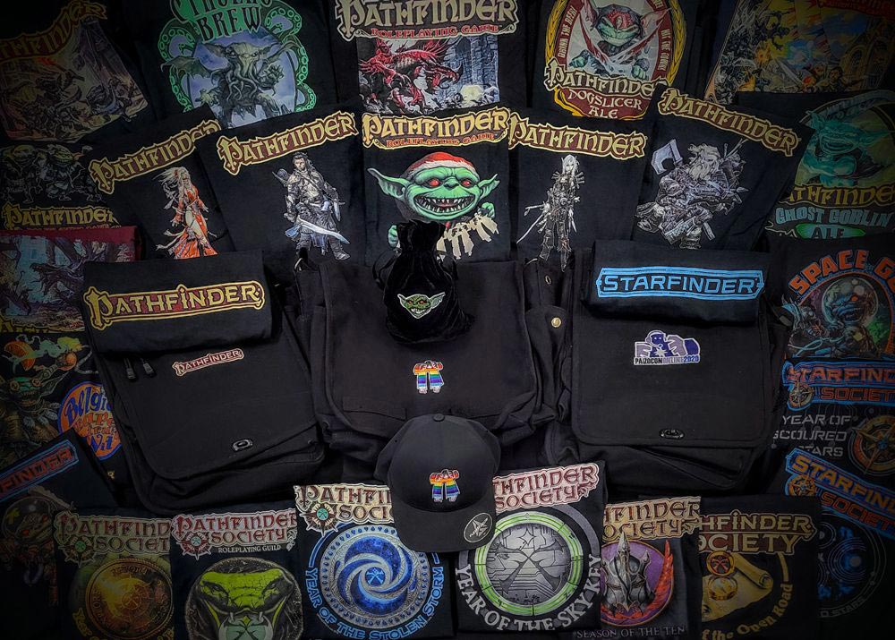 Off World Design's Paizo branded merchandise, Pathfinder and Starfinder Logo T-shirts, a goblin dice bag, Paizo's pride golem on a black messenger bag and black baseball cap.