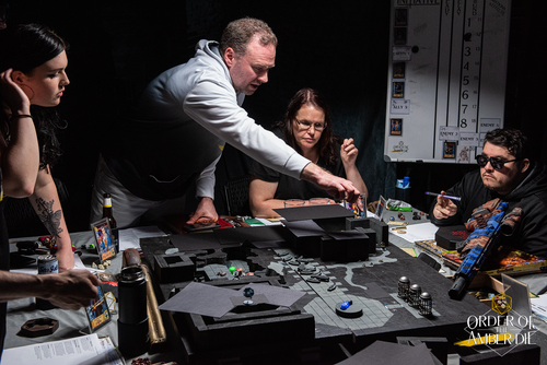 Order of the Amber Die: Players sitting and standing around a gaming table with a covered map