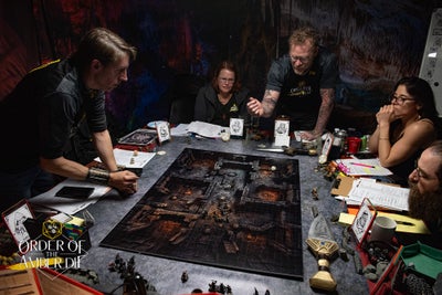 The Order of the Amber Die tabletop gaming group sitting around a gaming table with a large map and props in the center of the table.