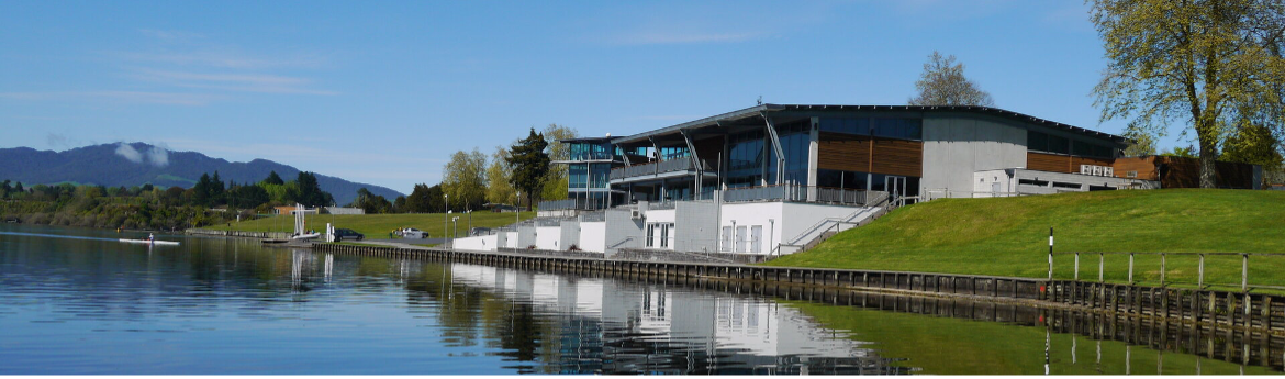 The Don Rowlands Centre in New Zealand. A wide low building sitting on the edge of a lake on a clear day with blue skies.