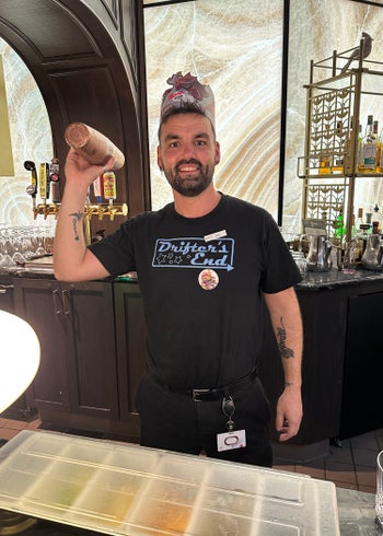A photo of a bartender wearing a Drifter's End T-shirt, a black t-shirt with blue text, shaking up a cocktail with one hand