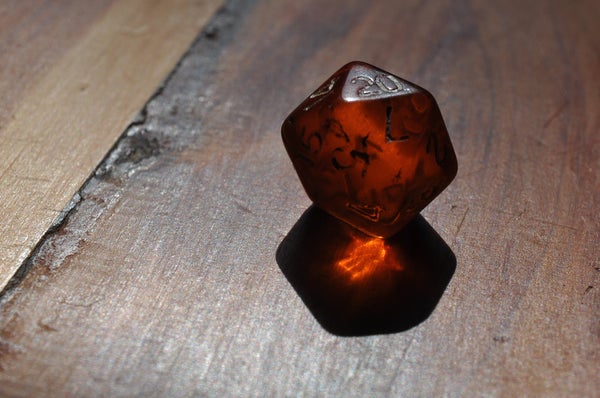 Order of the Amber Die: A semi-opaque amber colored dice sitting on a wooden table